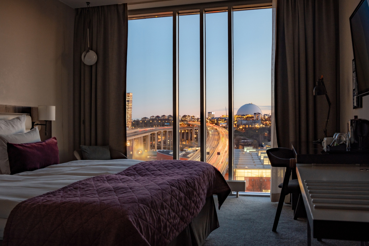 Hotel room at Clarion Hotel Stockholm with floor-to-ceiling windows and a panoramic evening view over the Stockholm skyline.