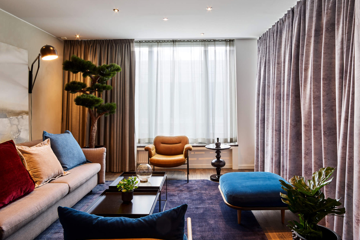 Living room of the Söder Suite at Clarion Hotel Stockholm, with a sofa, leather armchair, blue ottoman, and decorative tree.