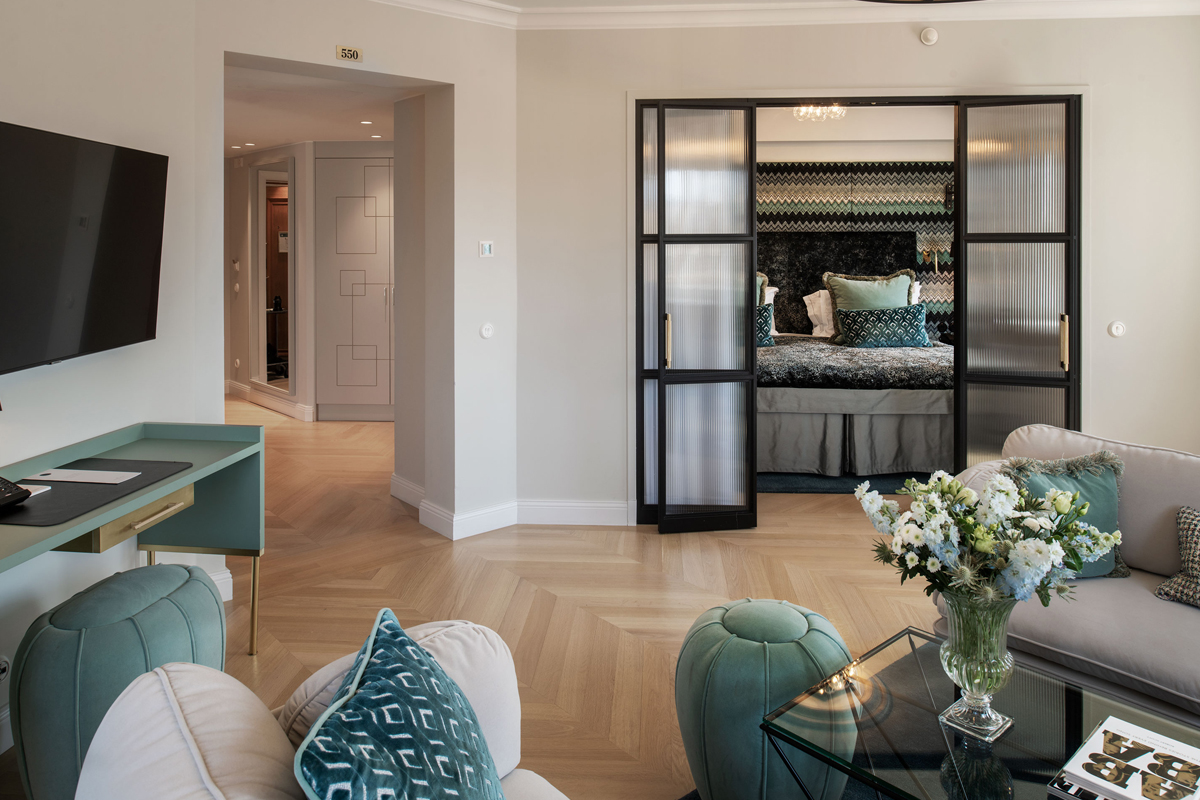 Living room of a fifth-floor suite at Grand Hôtel Stockholm, with teal accents, glass partition doors, and a view into the adjoining bedroom.