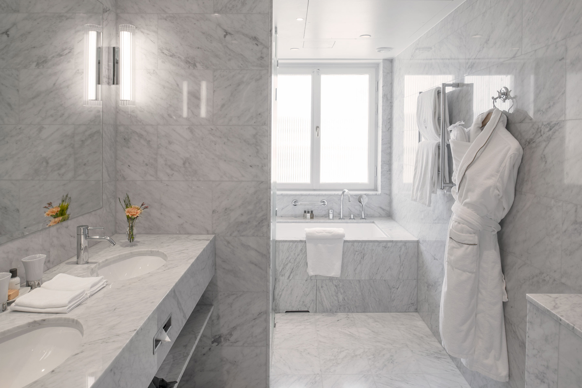 Marble bathroom in a suite at Grand Hôtel Stockholm, with a freestanding bathtub, double sink, and bathrobes.