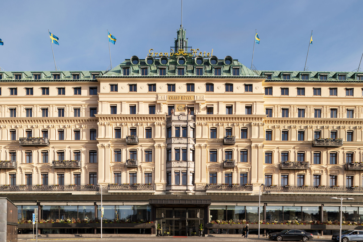 Front facade of Grand Hôtel Stockholm, a five-star landmark hotel on the Stockholm waterfront, with Swedish flags flying above the building.