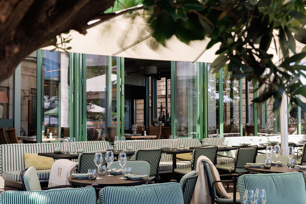Outdoor terrace of Grand Soleil restaurant at Grand Hôtel Stockholm, with striped seating and green-framed glass doors overlooking the waterfront.