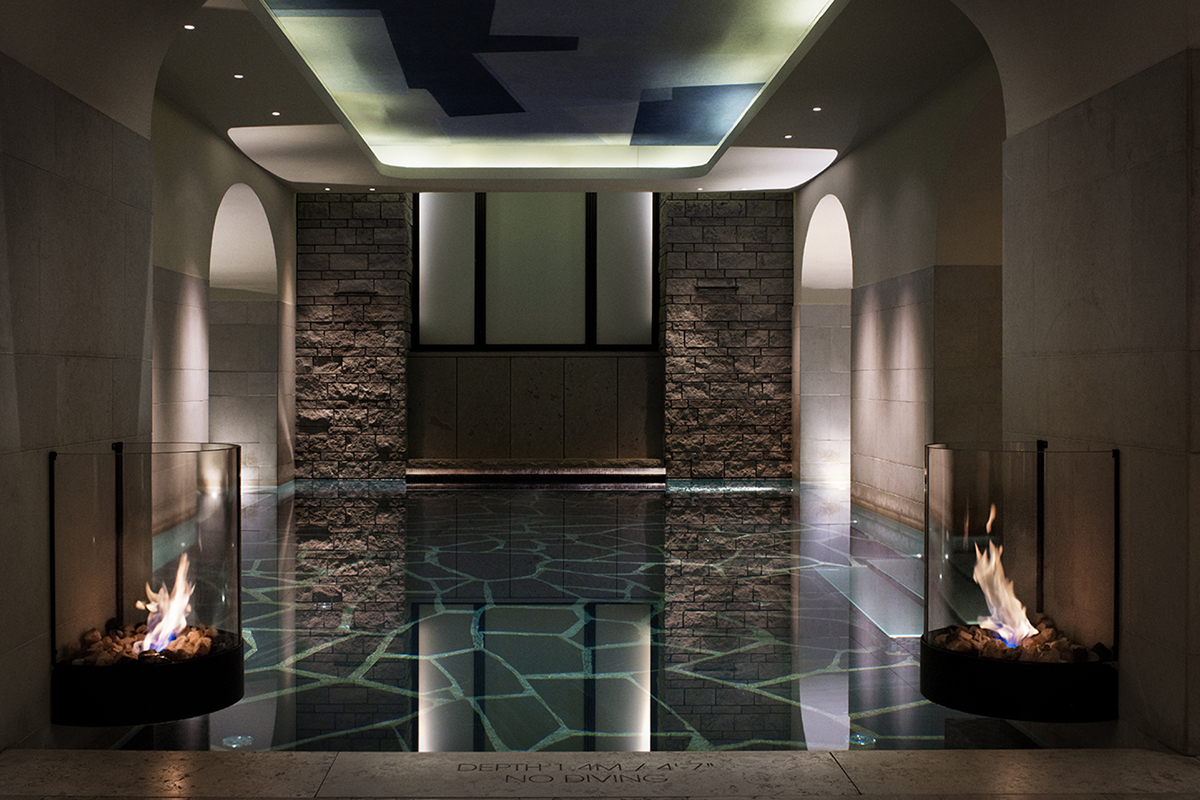 Indoor pool at the spa of Grand Hôtel Stockholm, with stone walls, open flames, and atmospheric lighting.
