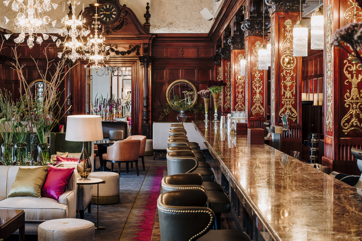 The Cadier Bar at Grand Hôtel Stockholm, with ornate dark wood panelling, a marble bar counter, and crystal chandeliers.
