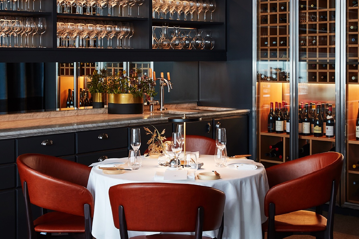 Dining table at the Seafood Gastronomy restaurant at Grand Hôtel Stockholm, with wine racks and glassware in an intimate dark-toned setting.