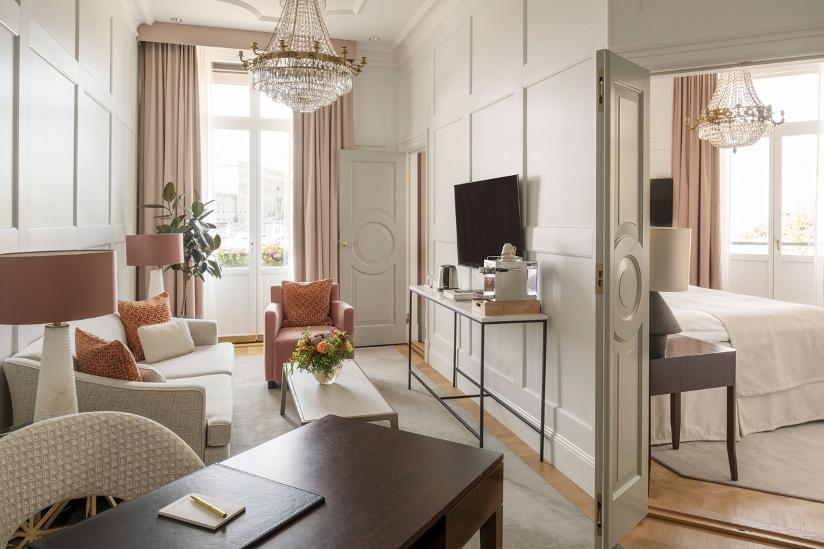 Sitting room and bedroom of a Superior Suite at Grand Hôtel Stockholm, with crystal chandelier, pink accents, and waterfront views.