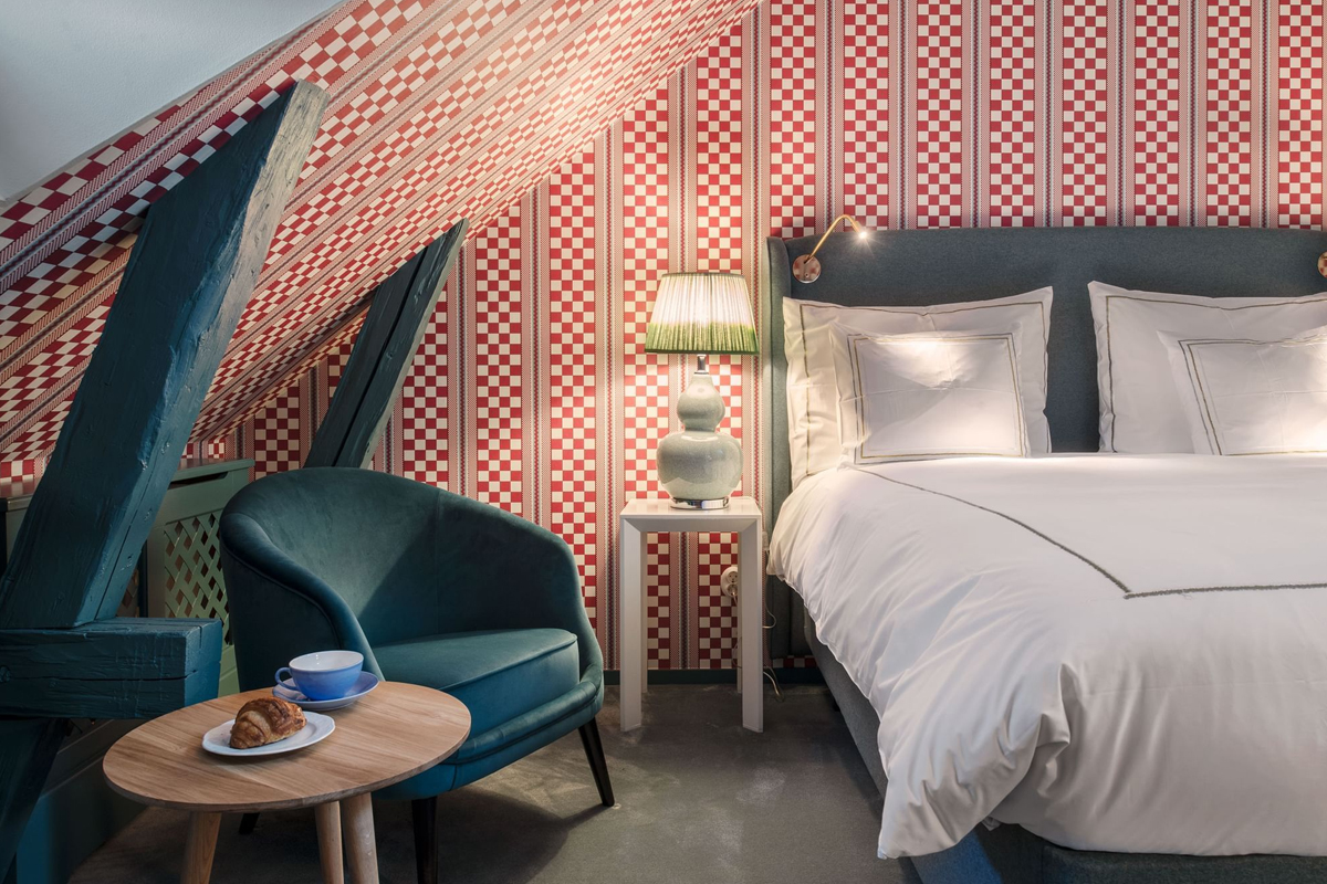 Unique room at The Sparrow Hotel in Stockholm, with bold red patterned wallpaper, exposed roof beams, and a double bed on the top floor.