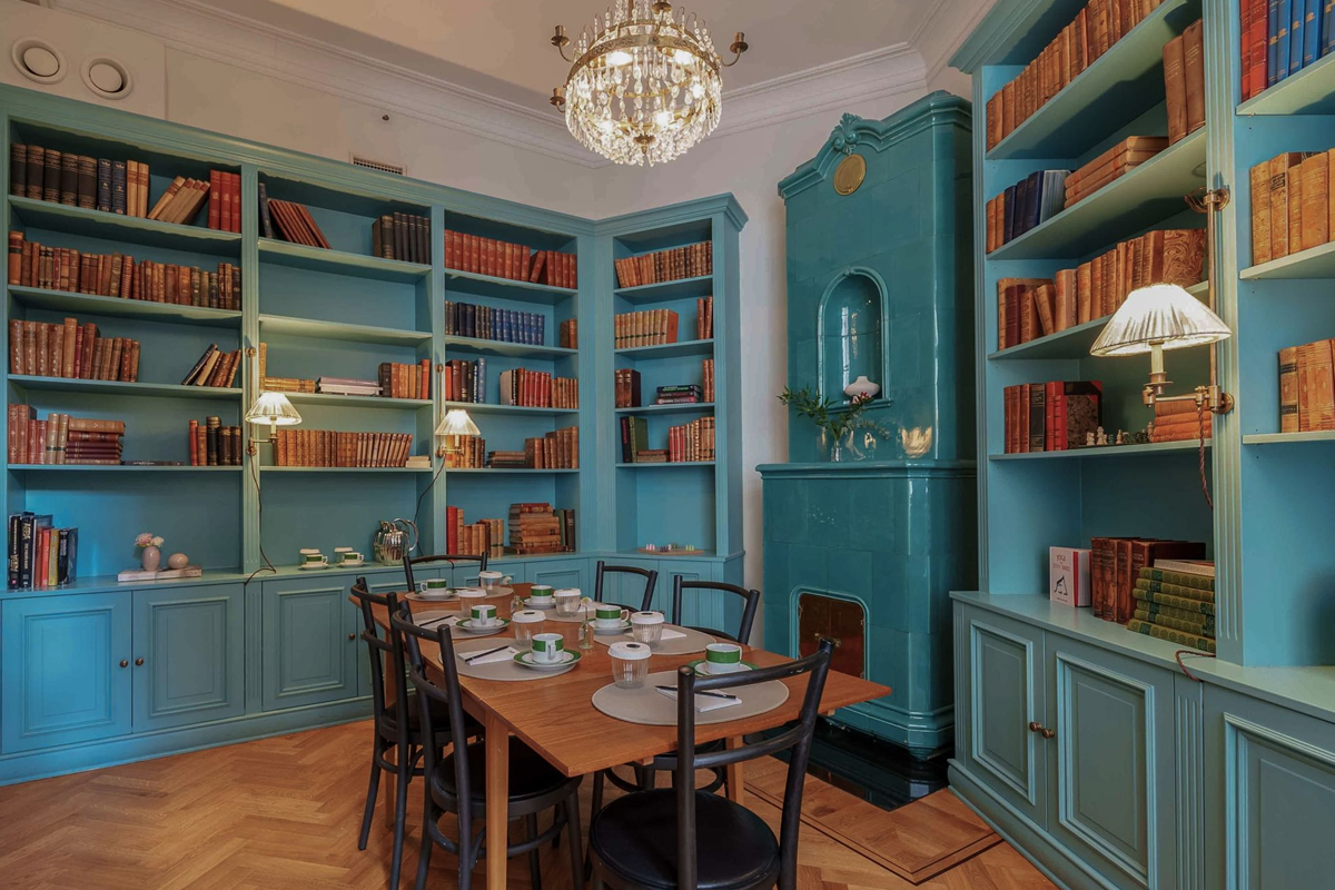 Library and private dining room at The Sparrow Hotel in Stockholm, with floor-to-ceiling teal bookshelves, chandelier, and a dining table for six.