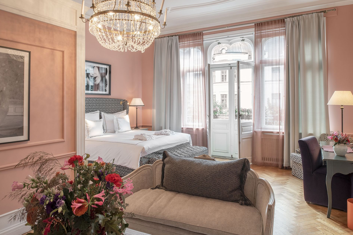 La Suite Rose at The Sparrow Hotel in Stockholm, with pink walls, crystal chandelier, king-size bed, and large arched windows facing the street.