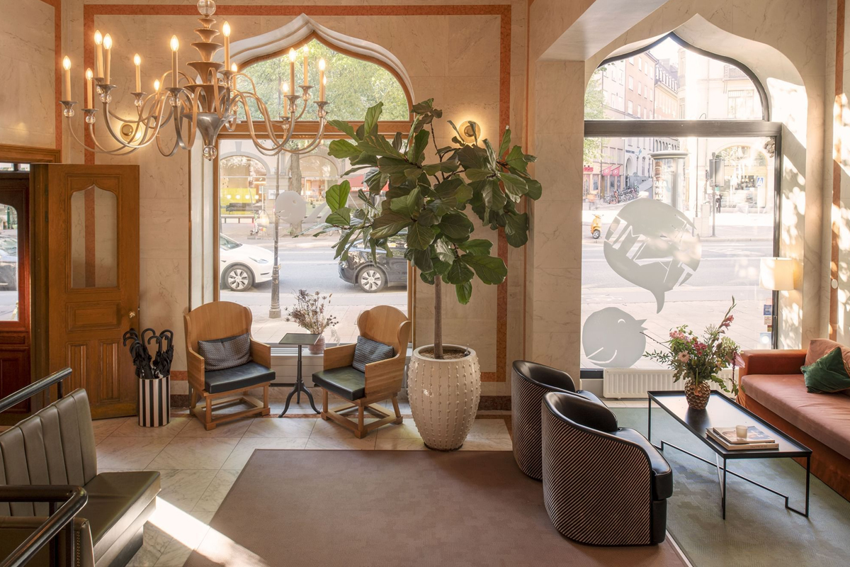 Reception and entrance lobby at The Sparrow Hotel in Stockholm, with ornate arched windows, eclectic seating, and views of Stureplan.