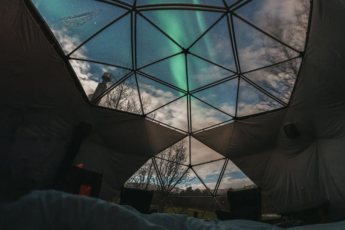Northern lights seen through the dome ceiling of an Aurora Igloo at Aera.
