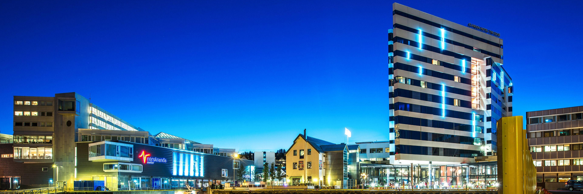Clarion Hotel The Edge lit up against a deep blue sky over the Tromso waterfront at dusk.