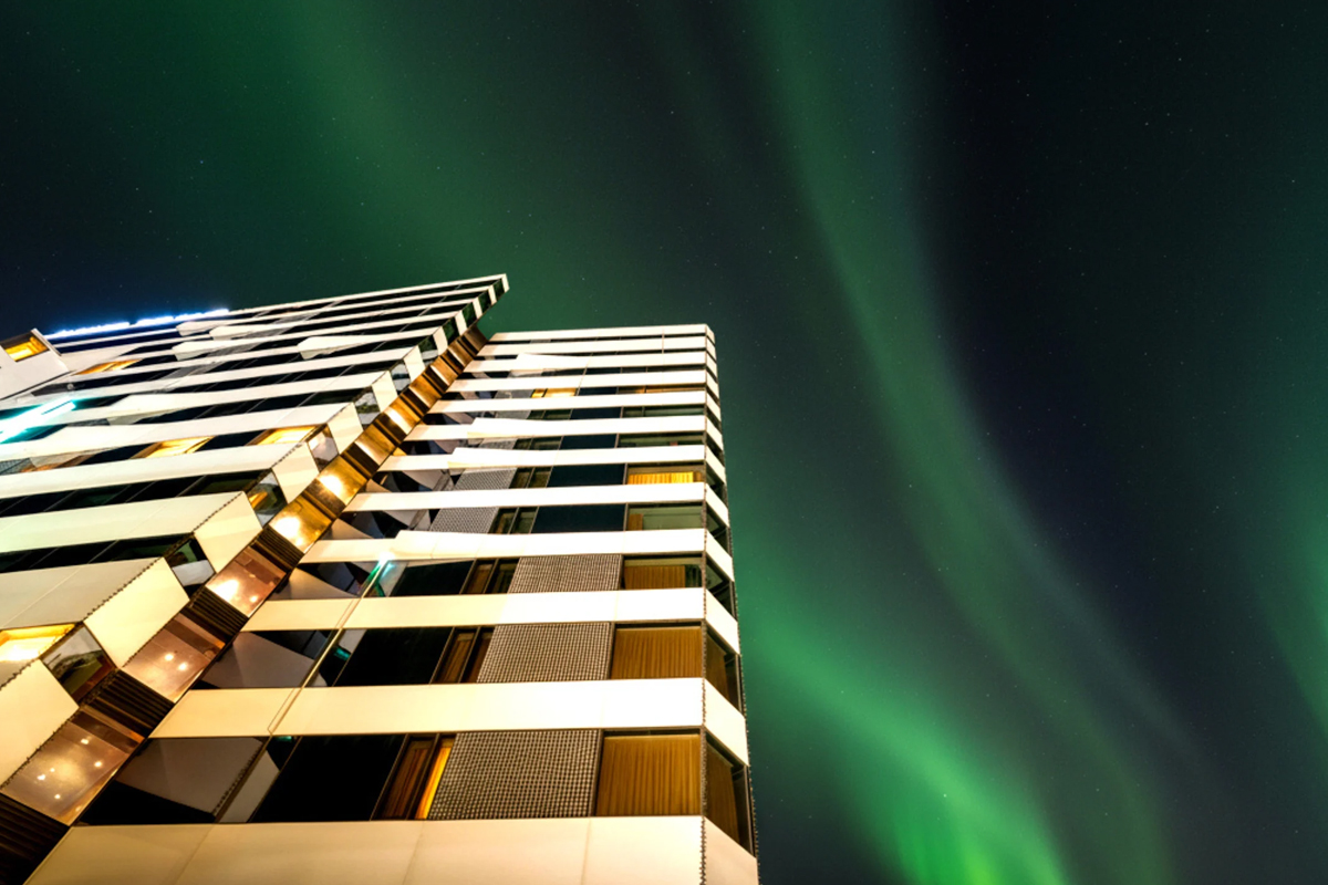 Green northern lights streak across the sky above Clarion Hotel The Edge in Tromso.