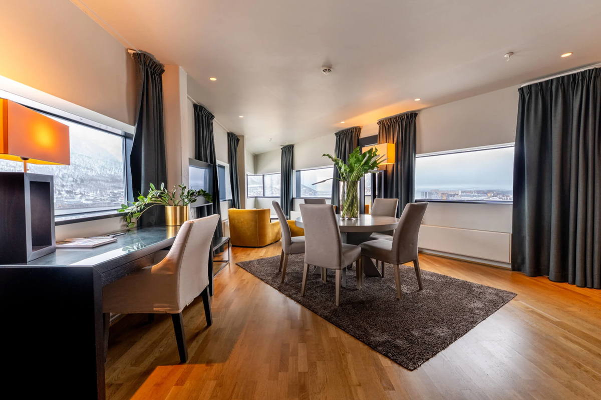 A suite lounge with dining table and mountain views through floor-to-ceiling windows at Clarion Hotel The Edge, Tromso.