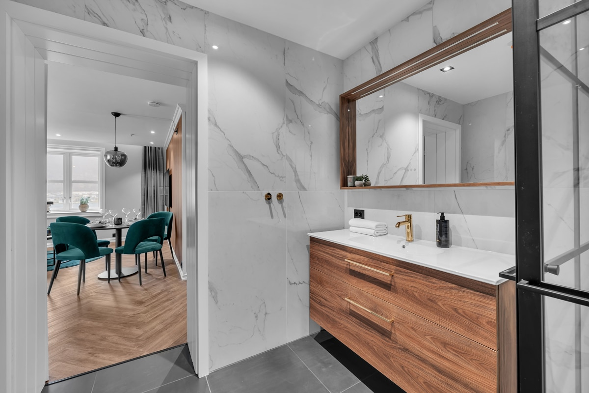 Marble bathroom at St. Elisabeth Hotel & Spa in Tromso, with a wood vanity and view to the dining area.