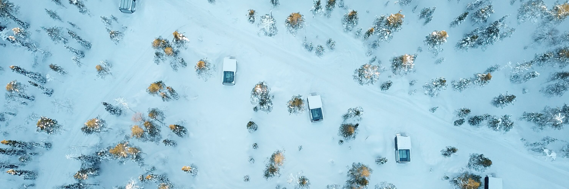 Aerial view of Arctic Skylight Lodge glass cabins set among snow-covered trees in the Ylläs region of Finnish Lapland.