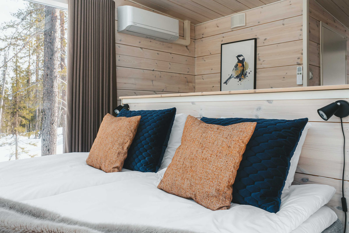 Bedroom inside a glass cabin at Arctic Skylight Lodge near Ylläs, with light wood walls, a king-size bed, and forest views.