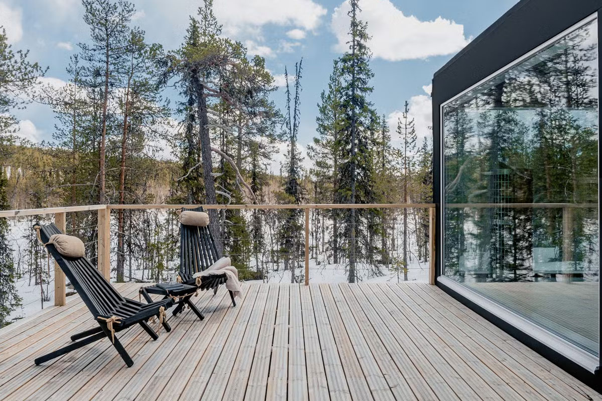 Outdoor terrace of a glass cabin at Arctic Skylight Lodge near Ylläs, with wooden deck chairs facing the Lappish forest.