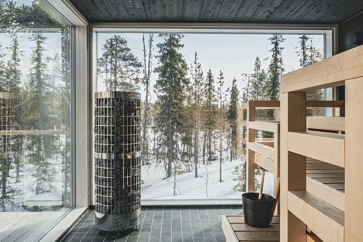 Interior of the glass-walled sauna at Arctic Skylight Lodge near Ylläs, with forest views through floor-to-ceiling windows.