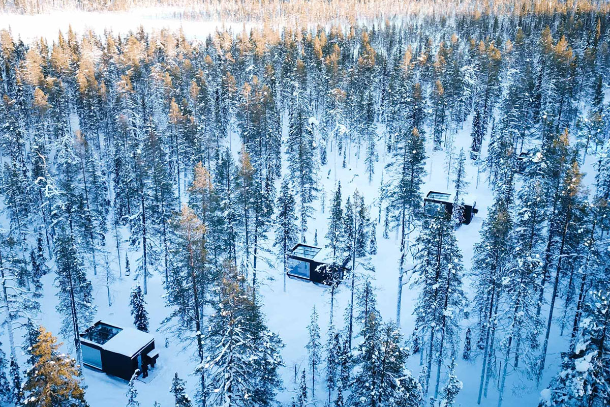 Glass cabins at Arctic Skylight Lodge spread through a dense snow-covered forest in the Ylläs region, Finnish Lapland.