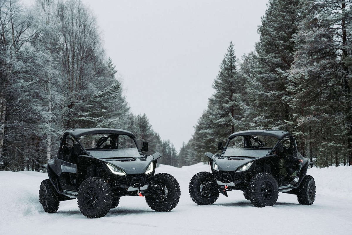 Two black ATV buggies parked side by side on a snowy forest road during a winter ATV tour in Lapland.