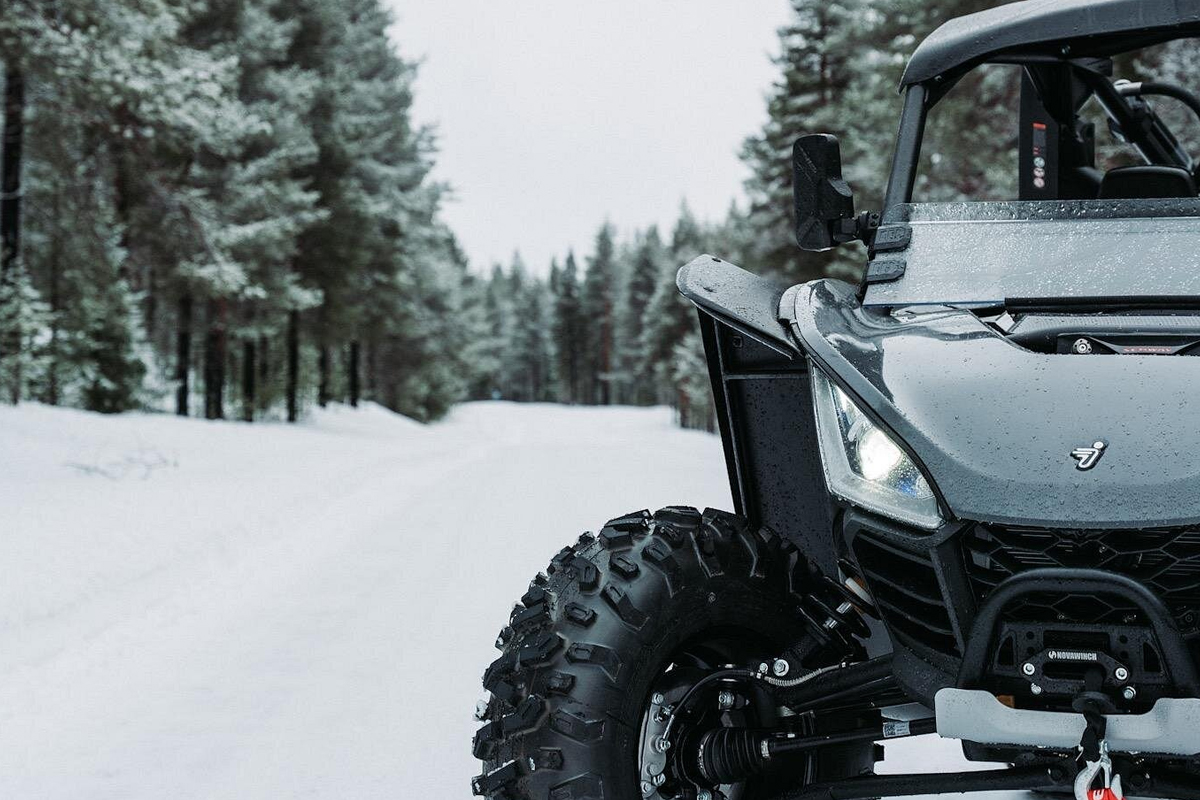 Close-up of a black ATV buggy headlight and front wheel on a snowy forest trail in Lapland.