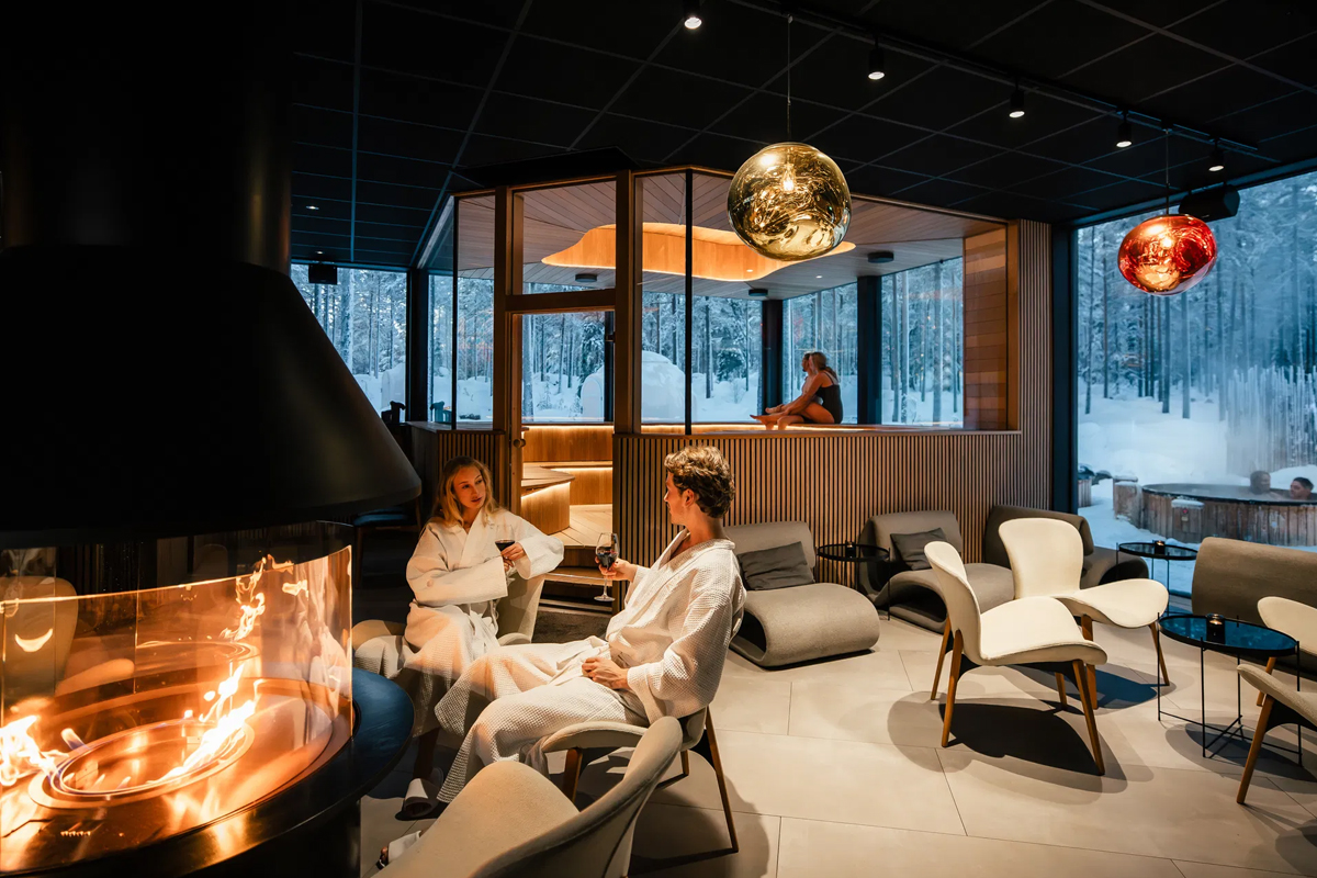 Guests in bathrobes relaxing by the fireplace at Arctic Forest Spa lounge.