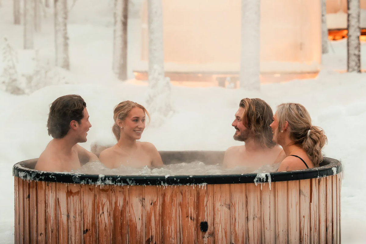 Guests in an outdoor wooden hot tub at Arctic Forest Spa, surrounded by snow.