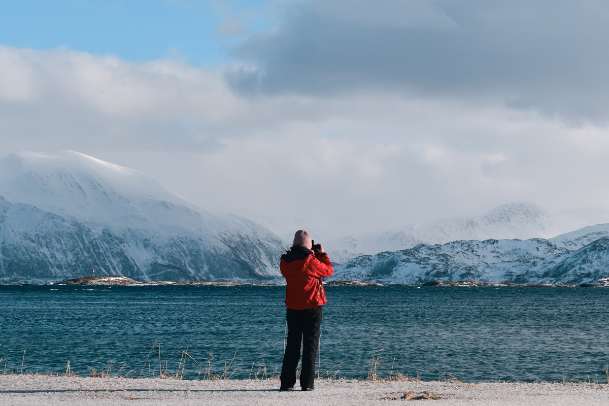 Traveler photographing snow capped mountains along an Arctic fjord. Photo: Joona.