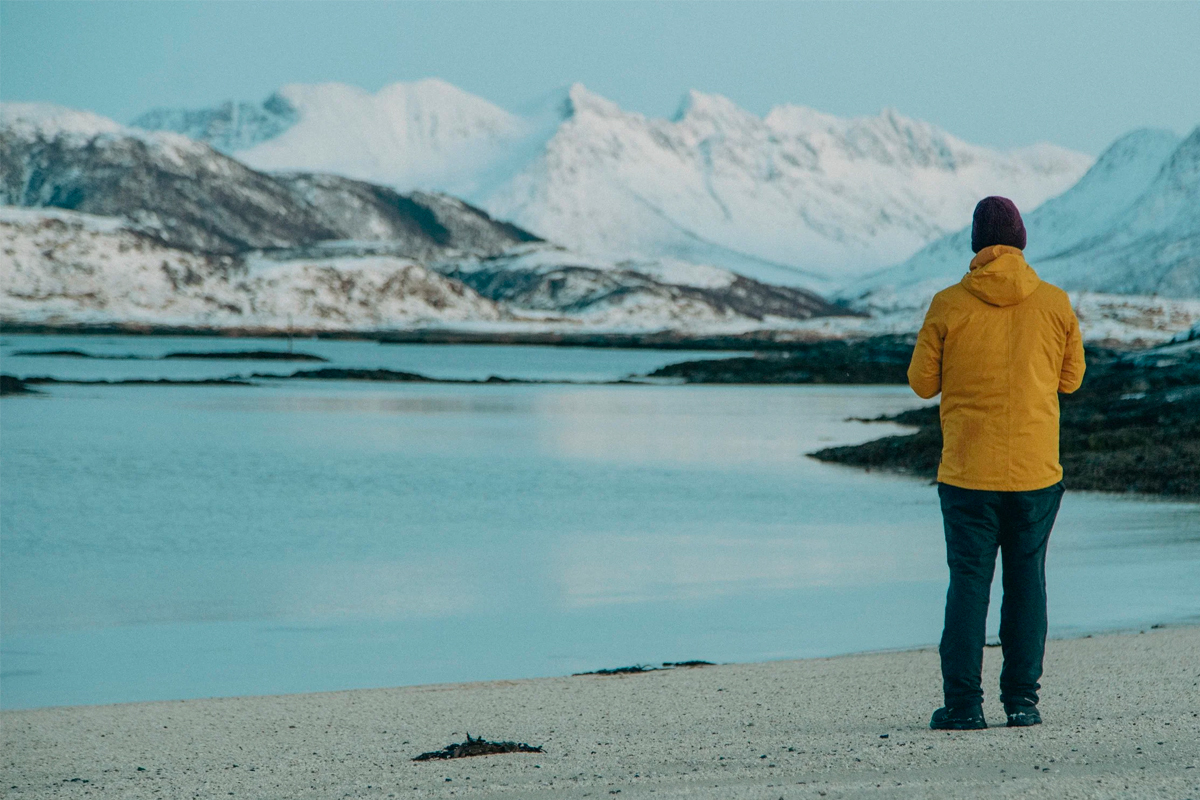 Traveler in a yellow jacket looking out over a calm Arctic fjord. Photo: Northern Soul Adventures.