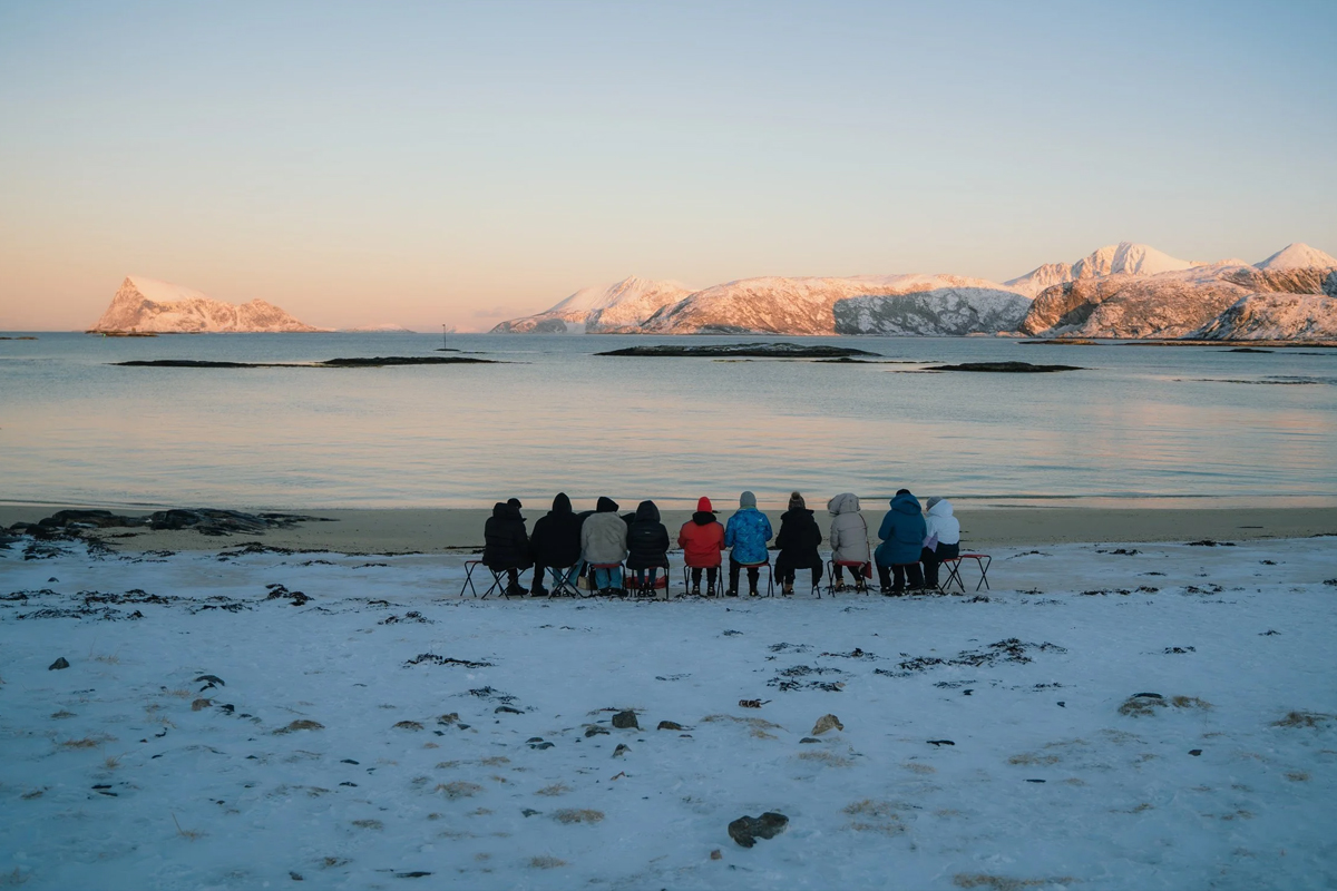 Group seated on the shore watching the sunset over an Arctic fjord. Photo: Northern Soul Adventures.