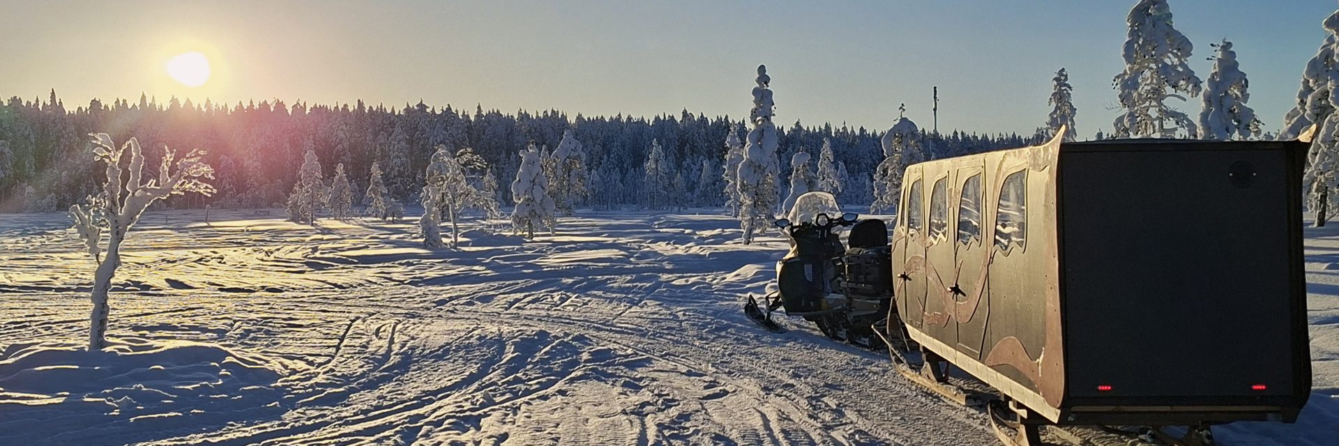 Heated sleigh and snowmobile on a frozen open landscape in Lapland at golden hour, snow-covered trees in the background
