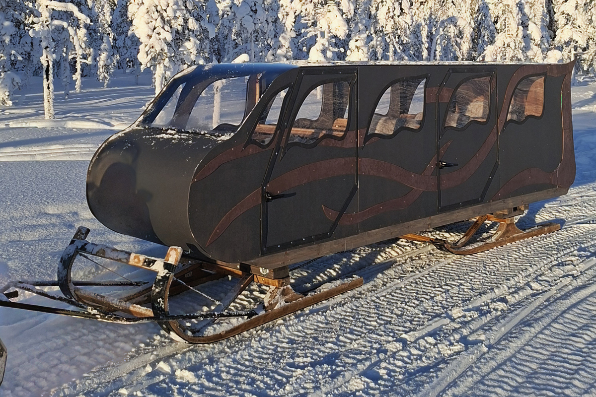 Exterior of a heated sleigh with curved wooden design details, parked on a snow trail in a winter forest