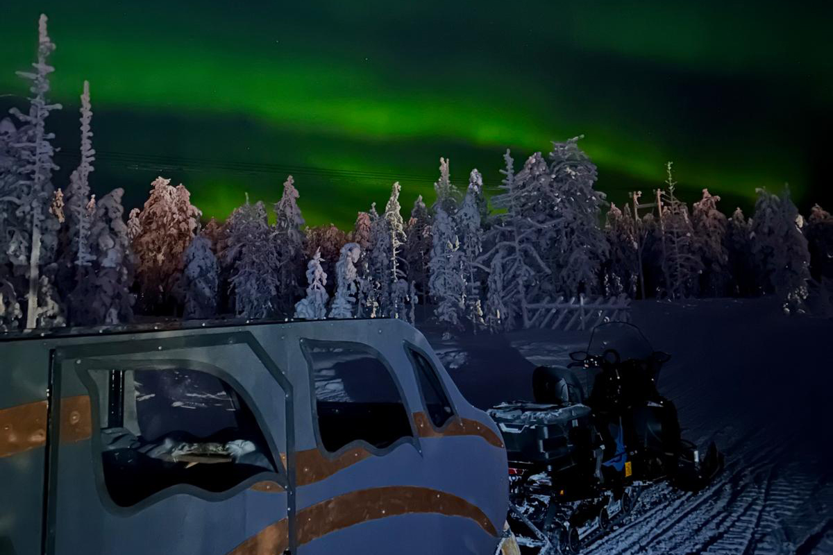 Heated sleigh and snowmobile parked under the northern lights in a snow-covered forest in Lapland
