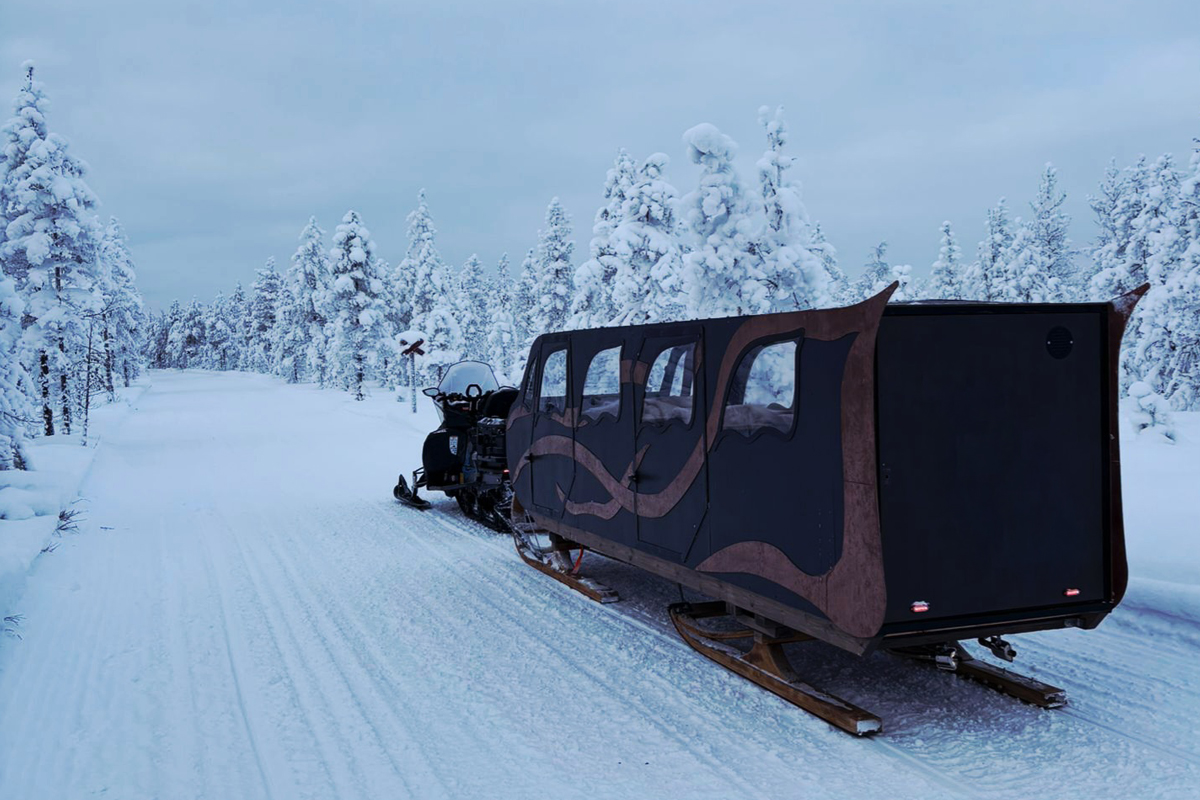Heated sleigh towed by snowmobile on a snow-covered forest trail in Lapland