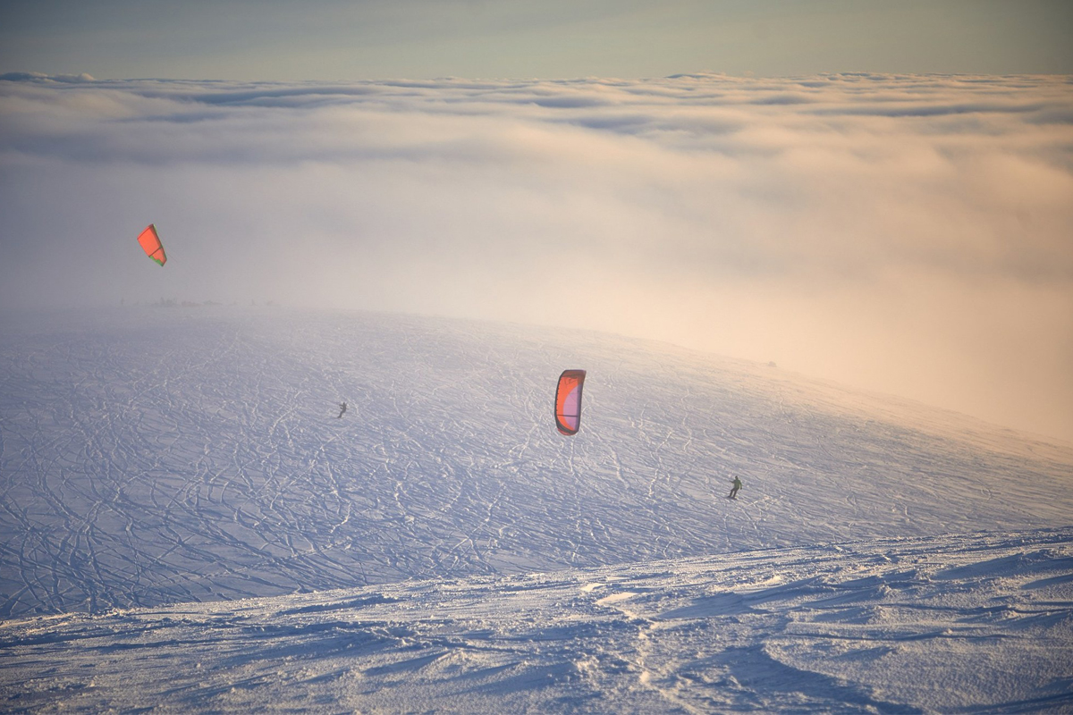 Two snow kiters cross a vast open snowfield above the clouds during a snow kiting session in Lapland.