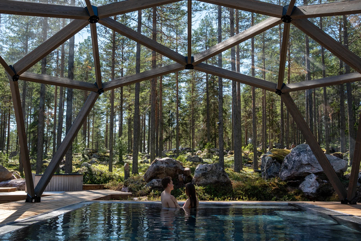 Couple relaxing in a heated pool beneath a timber dome in the forest at Invisible Forest Lodge