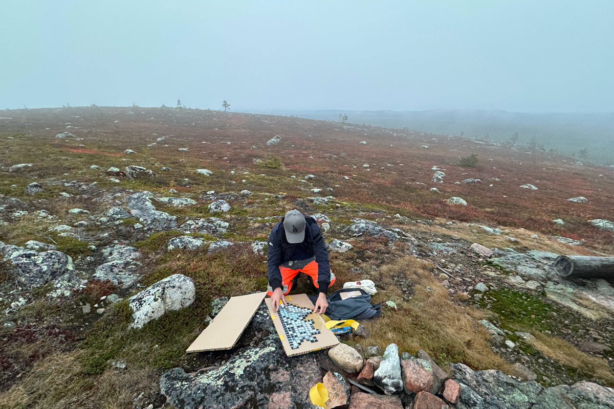 Artist assembling a pixel mosaic on cardboard on a misty autumn fell in Finnish Lapland ©Invader @invaderwashere