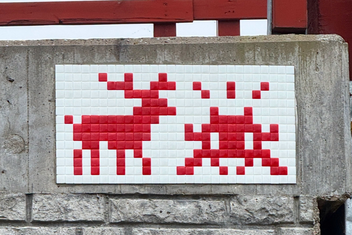 Red and white tile mosaic of a reindeer and a pixel invader on a concrete wall in Lapland ©Invader @invaderwashere