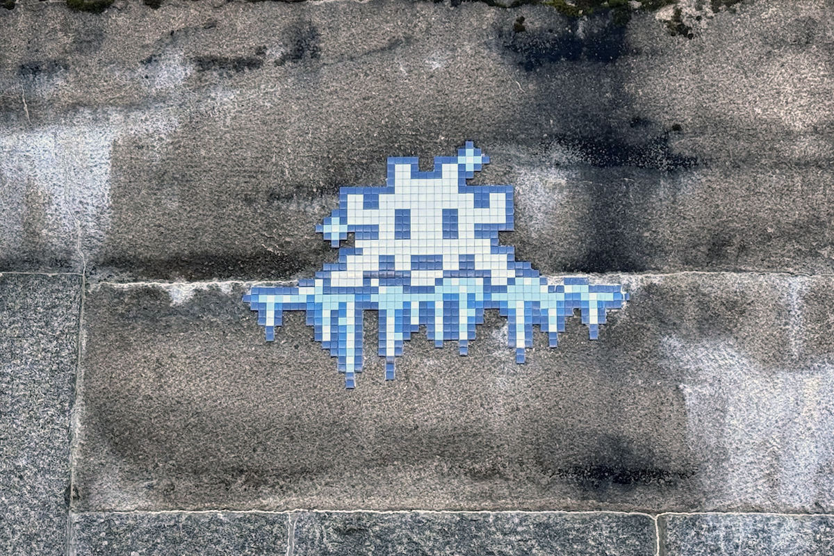 Blue and white tile mosaic of an invader with icicles on a weathered stone wall ©Invader @invaderwashere