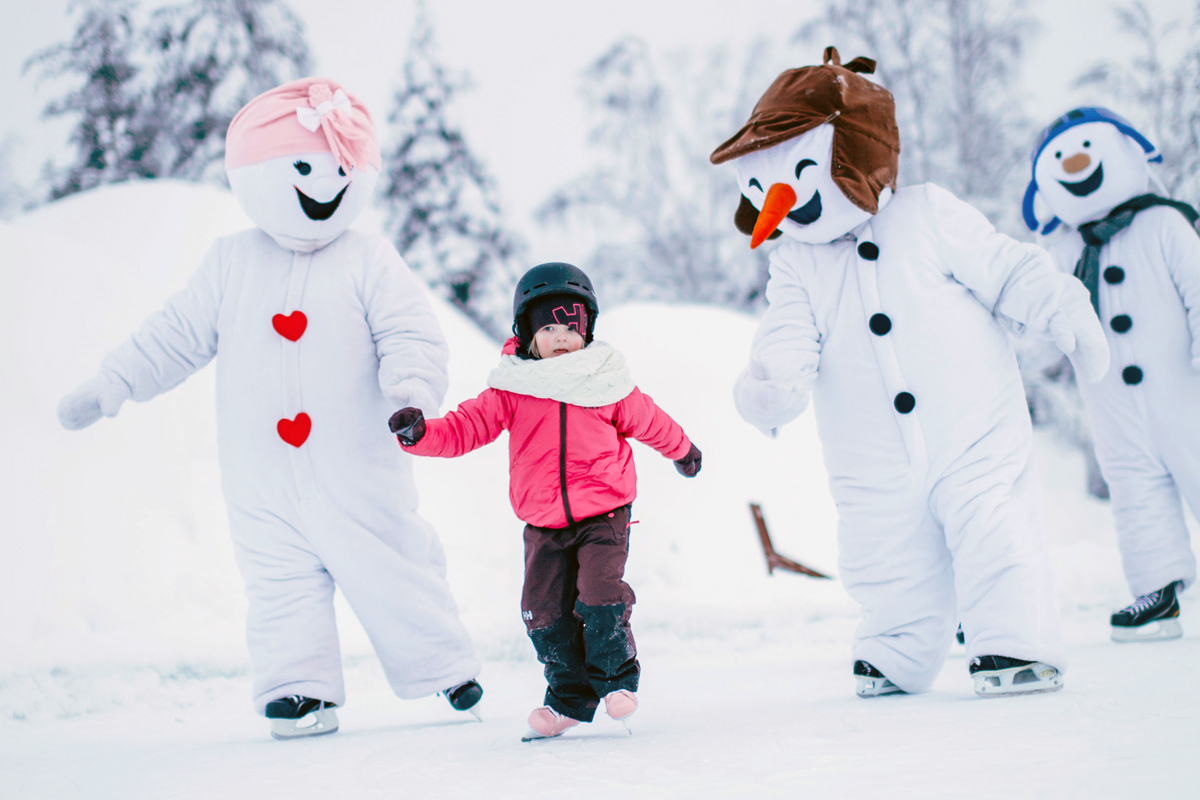 Toddler ice skating between smiling snowman characters on a snowy rink in Lapland
