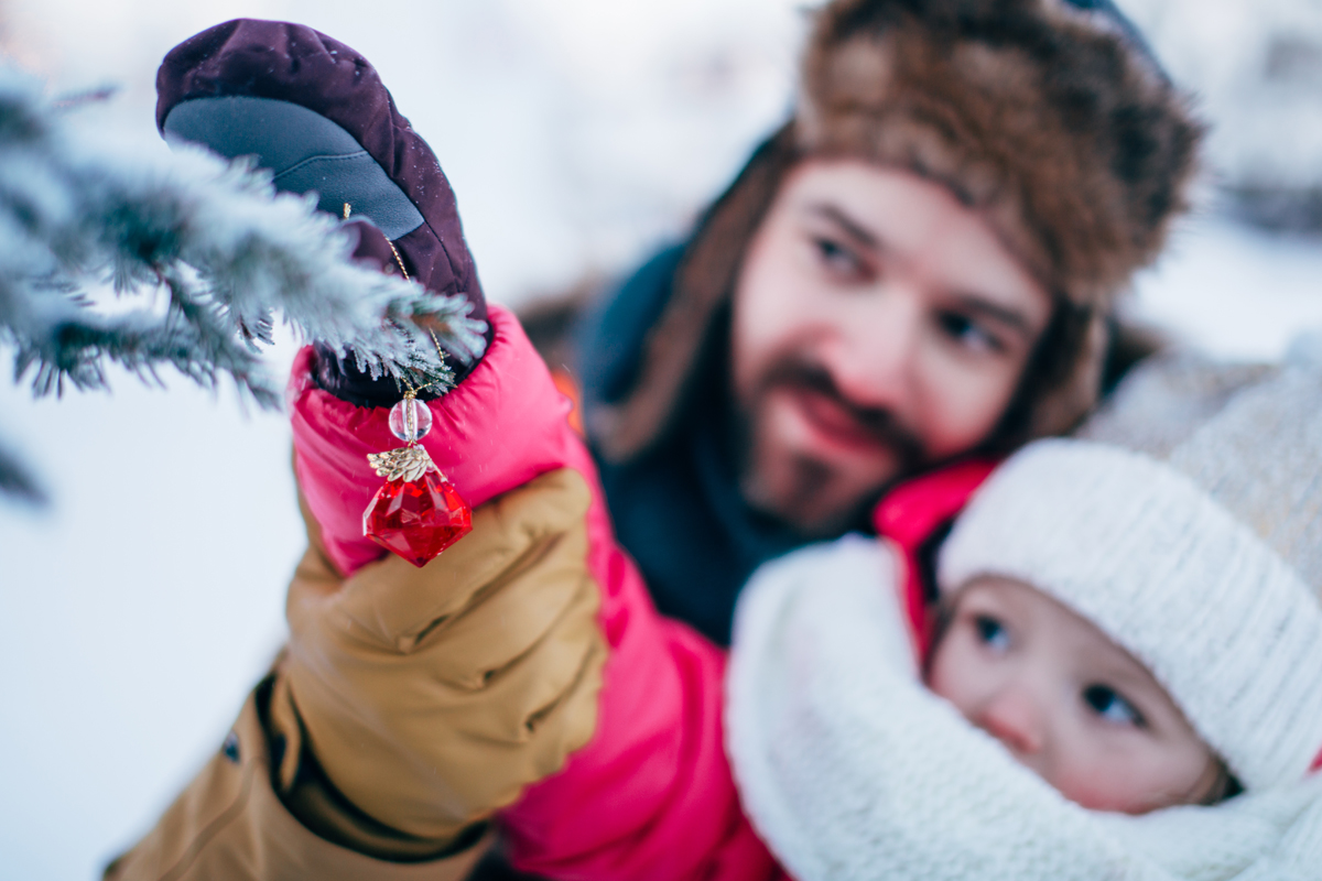 Father and toddler hanging a red ornament on a frosted fir tree in snowy Lapland