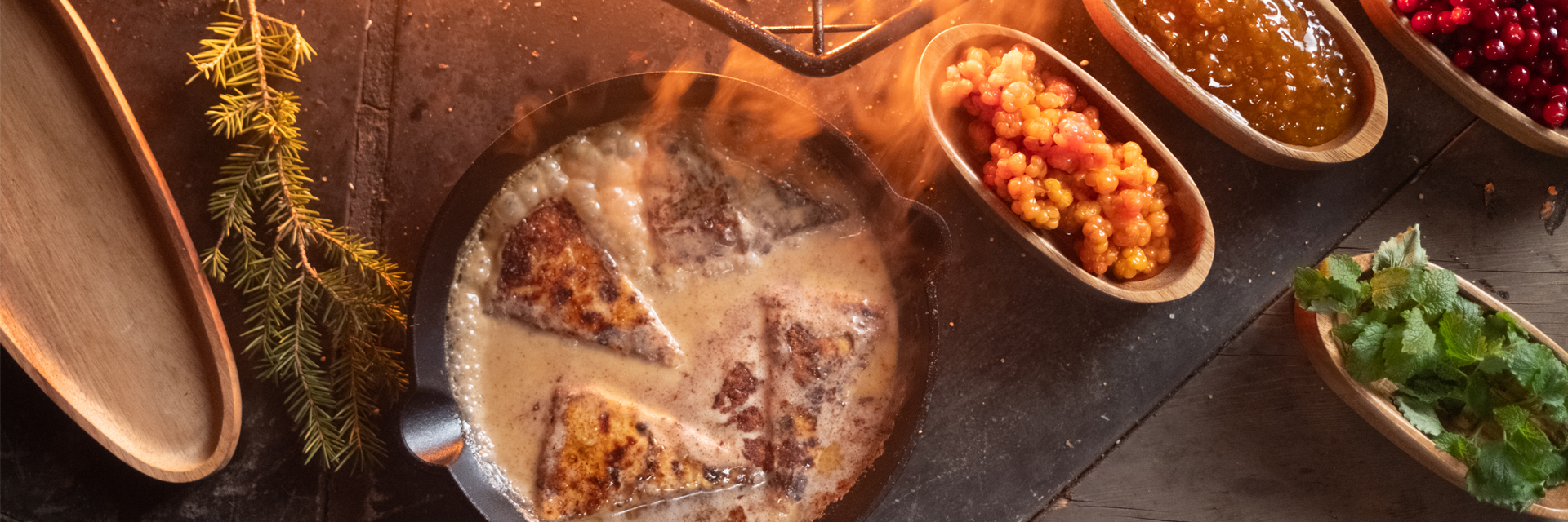 Pan-fried Finnish squeaky cheese served with cloudberries, lingonberry jam and fresh herbs in wooden bowls, Lapland