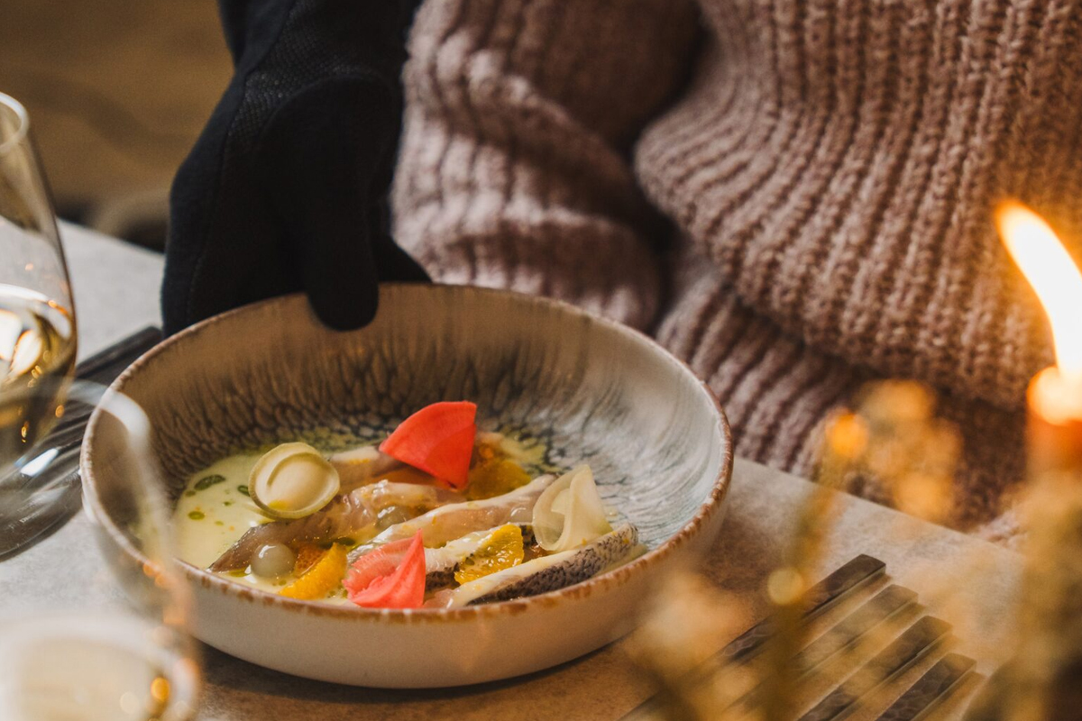 Elegantly plated Arctic fish dish with citrus and pickled vegetables, served in a ceramic bowl at Restaurant Aanaar, Inari