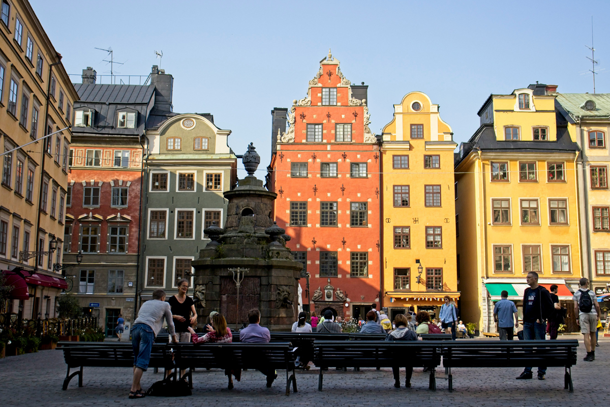 Stortorget square in Gamla Stan, Stockholm, with colourful historic facades and people seated on benches in summer.