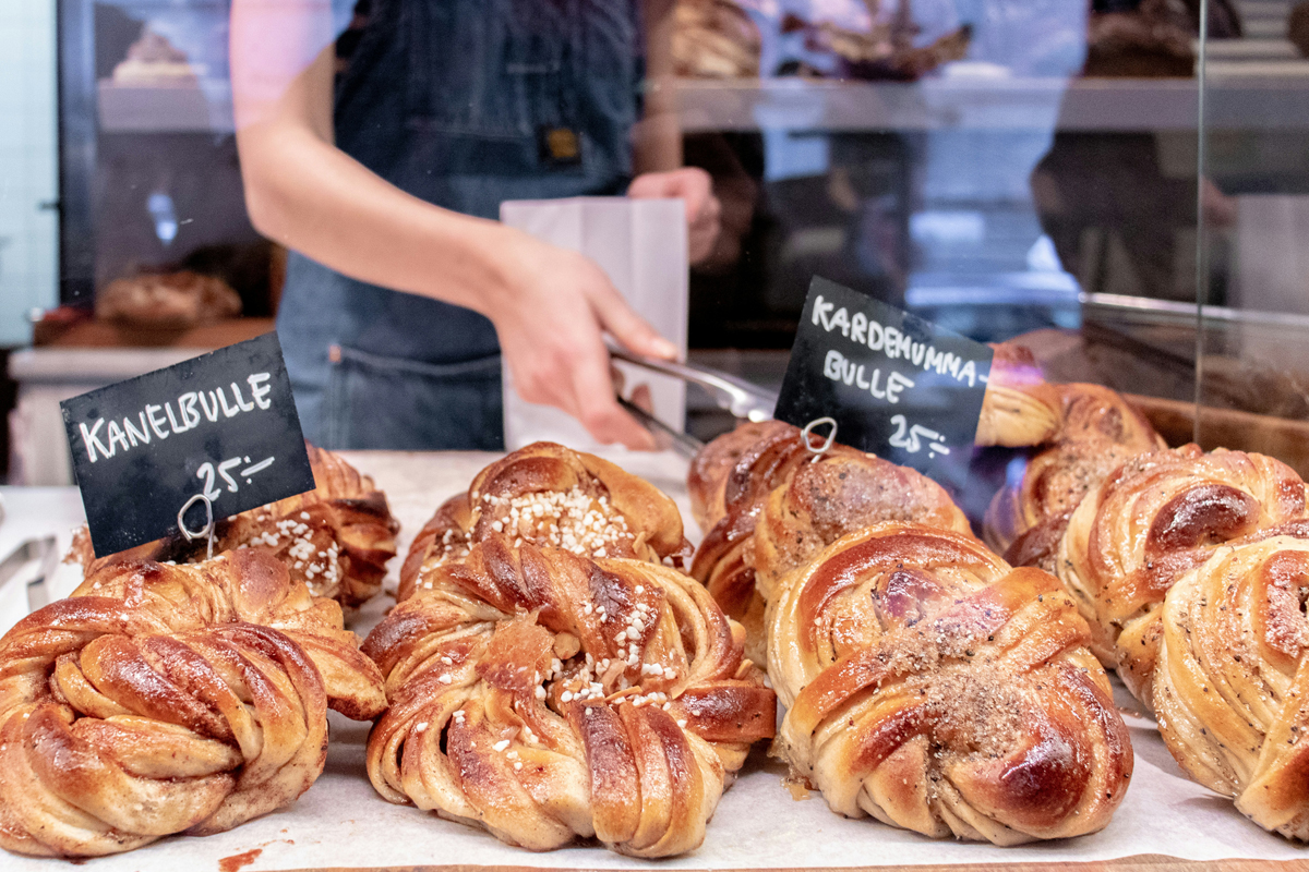 Kanelbullar and cardamom buns on a bakery counter in Stockholm, with handwritten price signs in Swedish.
