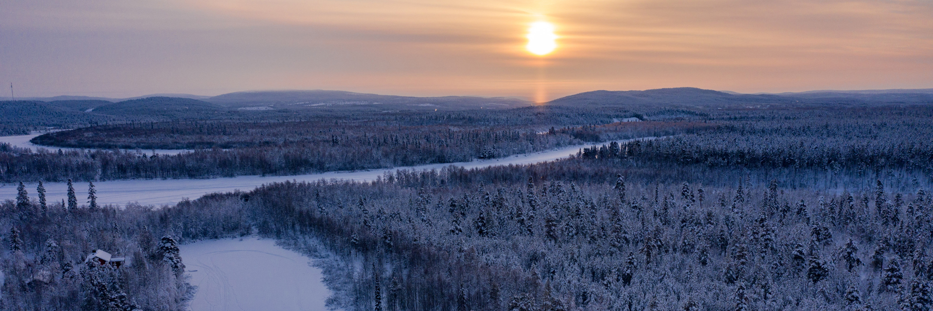 Aerial panorama of snow-covered forest and a frozen river under a low winter sun, Ivalo, Finnish Lapland