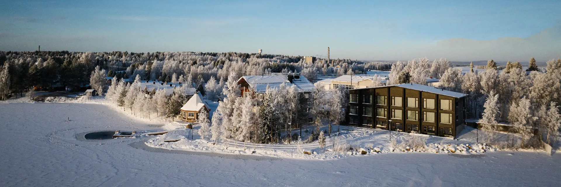 Aerial view of Jauri Resort on the shore of a frozen lake, surrounded by frost-covered trees on a clear winter day, Kemijärvi