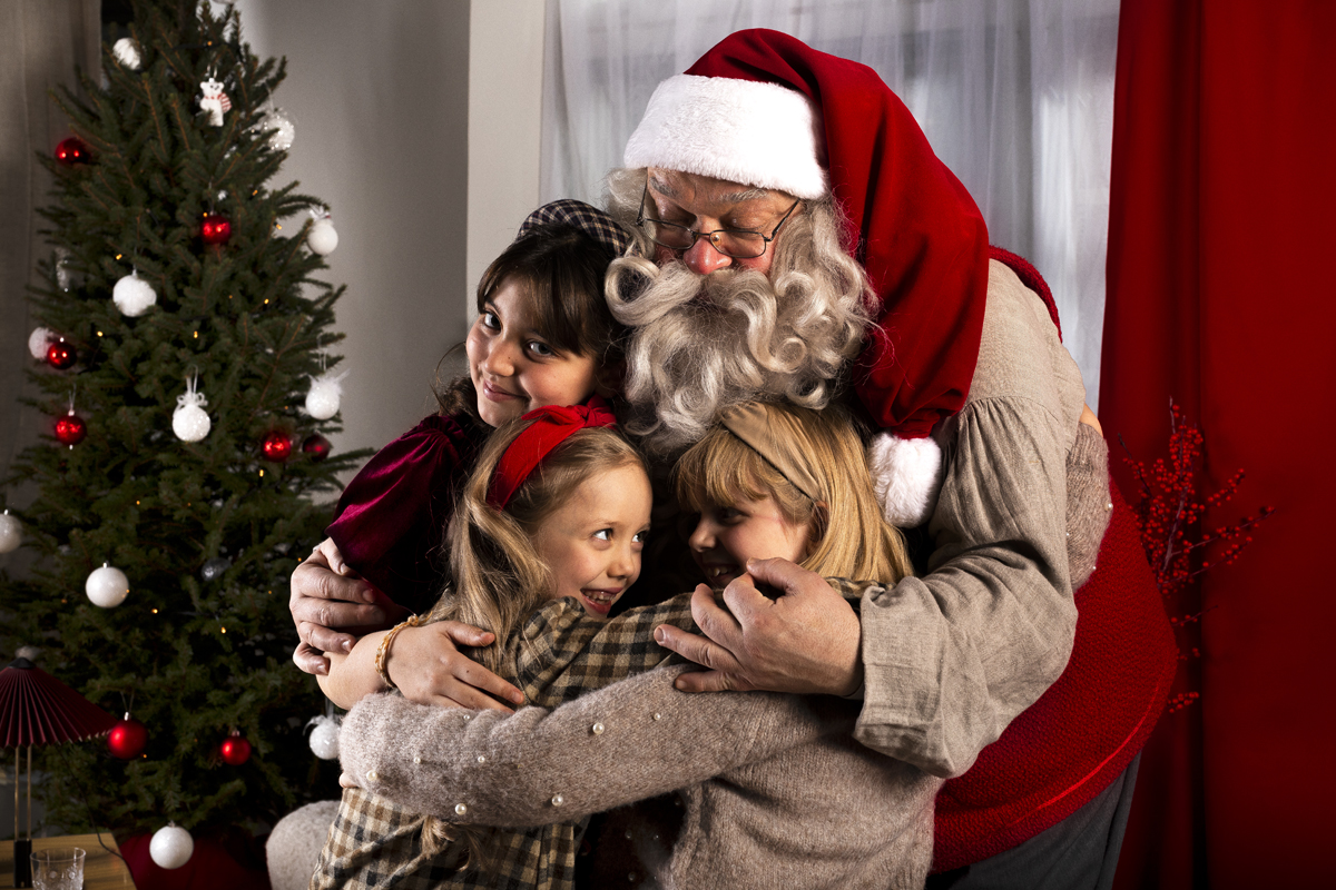 Santa Claus hugging three children by a Christmas tree during a private family visit in Lapland.