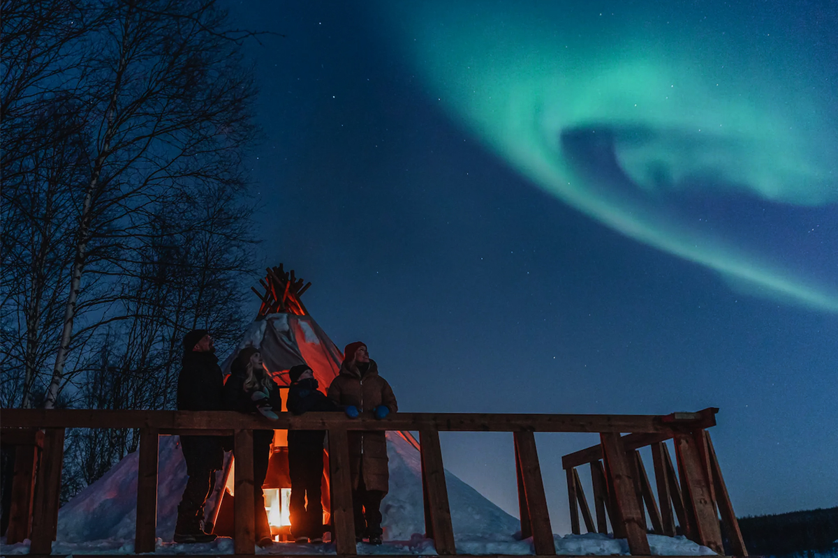 Family watching the Northern Lights from a wooden terrace in Finnish Lapland.